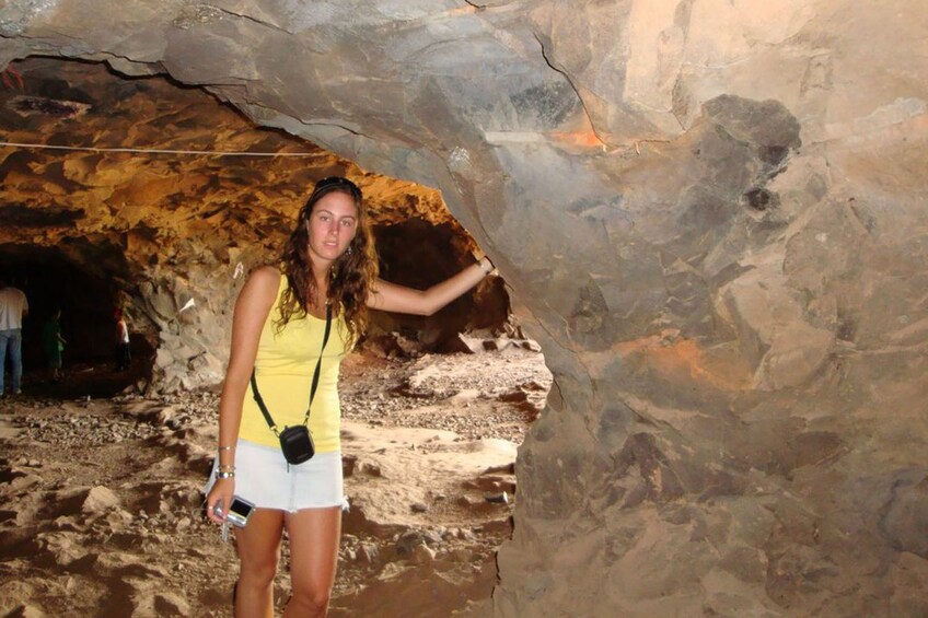 Une personne se tient dans une grotte dont les parois sont rocheuses, près de l’entrée de la grotte. 5
