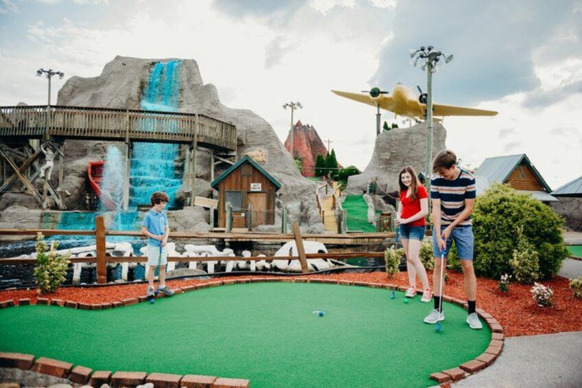 A miniature golf course with a green putting area, a waterfall, and a wooden structure. 2