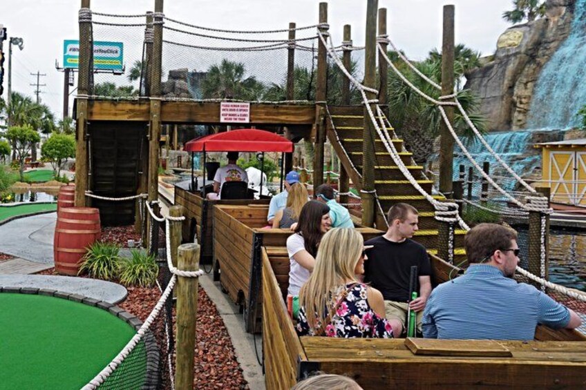 A wooden boat ride with passengers, a red canopy, and a rope bridge in the background. 5