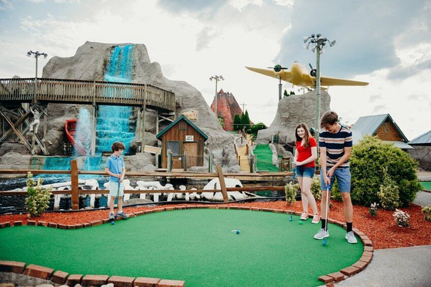 Un campo de mini golf con superficie de césped verde, un puente de madera y una cascada. 2