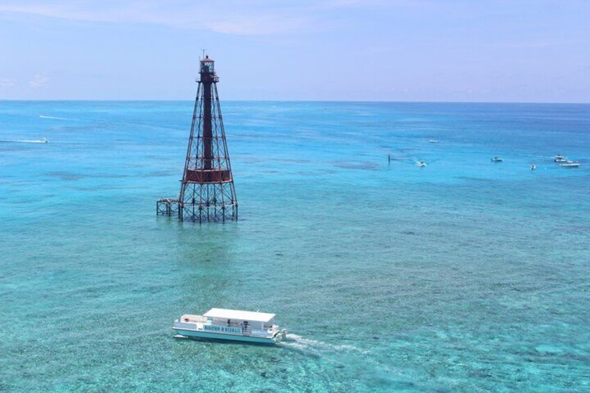 A boat on clear turquoise water, a tall structure in the distance, and a clear sky. 2