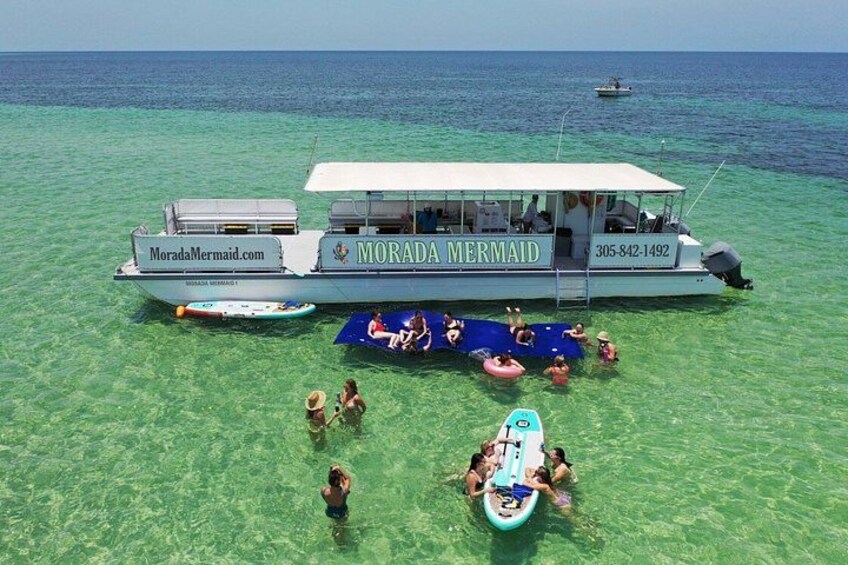 Un bote llamado 'Morada Mermaid' con gente en la playa y en el agua. 1
