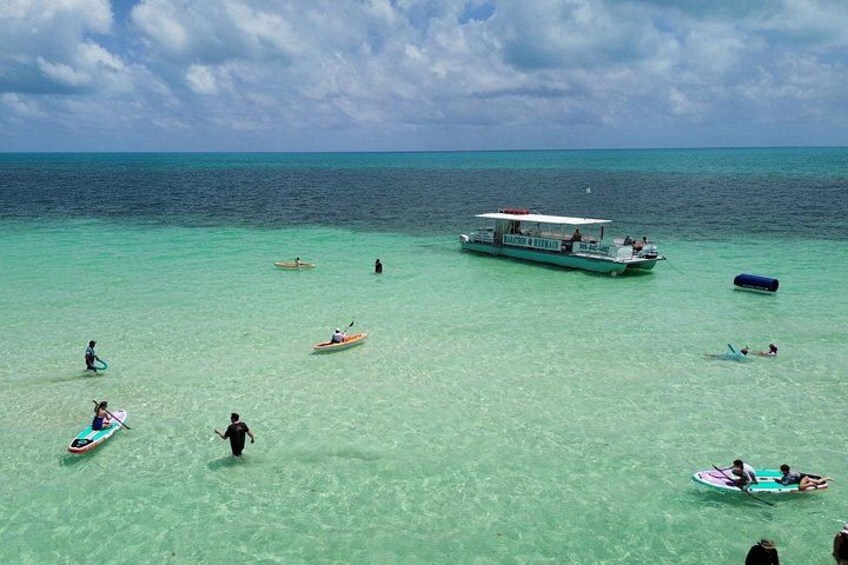 Una playa tropical con agua turquesa cristalina, un barco grande y varios botes pequeños y kayaks. 2