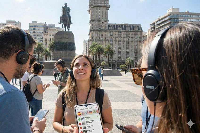 A group of people in a public square with a statue and buildings in the background. 1