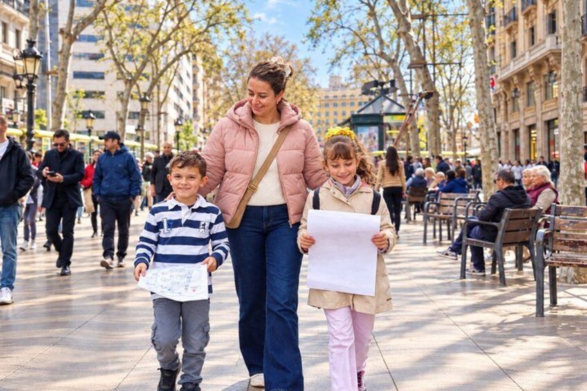 Una mujer caminando con dos niños, sosteniendo papeles, en una calle urbana con árboles y bancos. 1