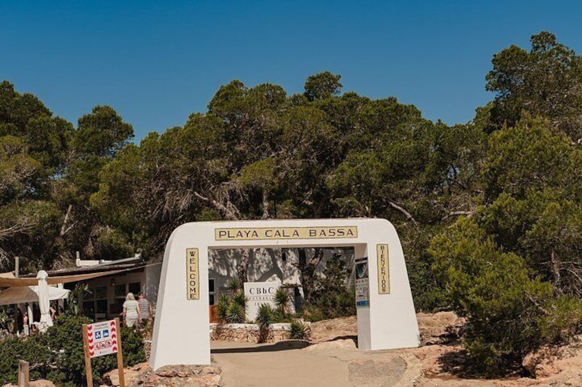 Un arco bianco con la scritta 'PLAYA CALA BASSA' e un segnale che indica un'area di parcheggio. 5