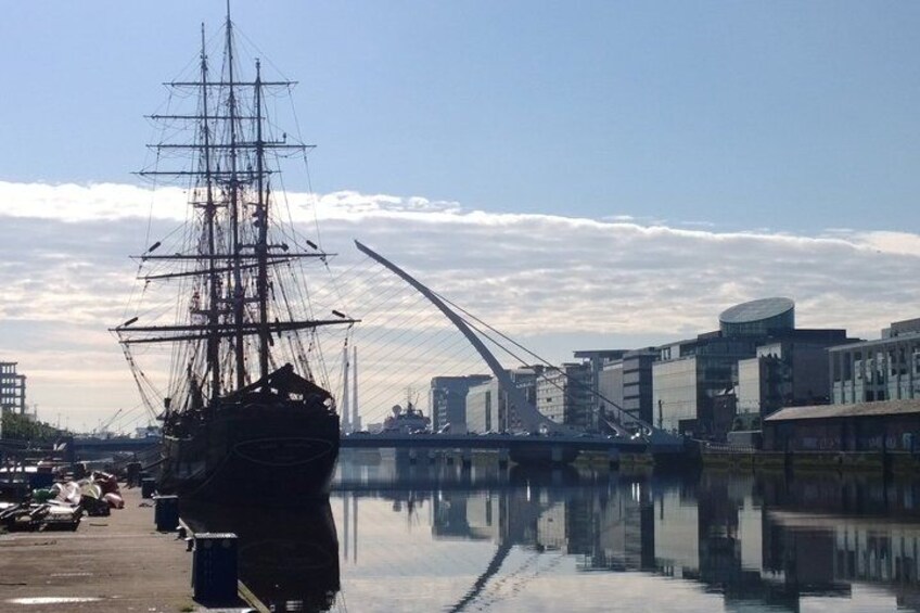 A tall ship docked at a harbor with modern buildings and a bridge in the background. 3