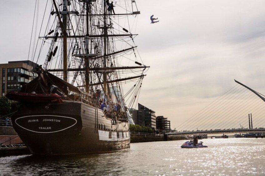 A tall ship named 'Jeanie Johnston' docked at a port with a modern bridge in the background. 5