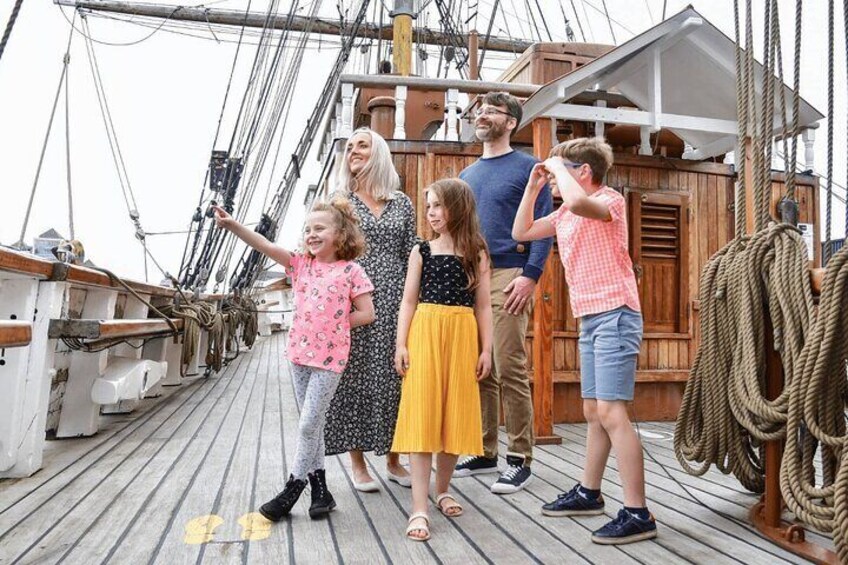 Eine Familie auf dem Holzboden eines Schiffes, mit Seilen und Takelage. 1