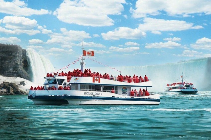 A boat named 'HORNBLOWER' with passengers wearing red jackets, a Canadian flag, and a waterfall in the background. 1