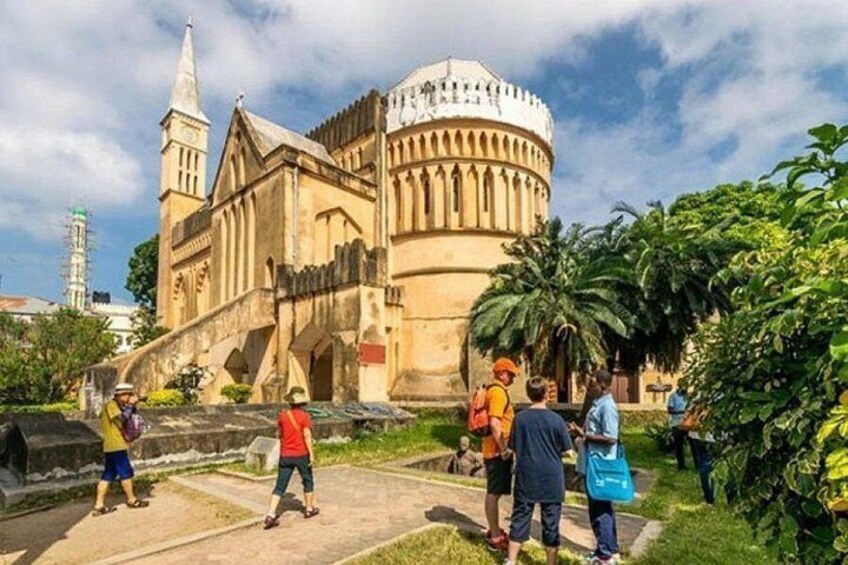 A historic building with a dome and a spire, surrounded by greenery and people. 3