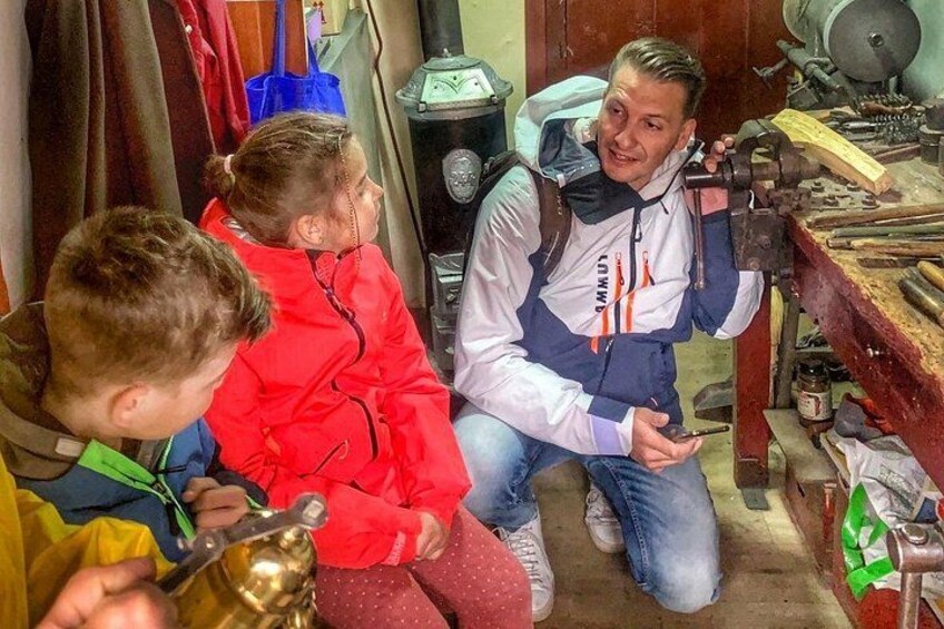 A workshop with tools and machinery, a person in a blue and white jacket, and two children in red jackets. 2