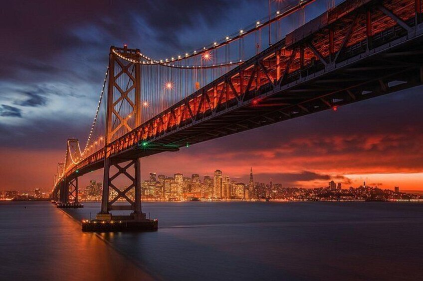 A bridge with lights, a city skyline, and a sunset. 5