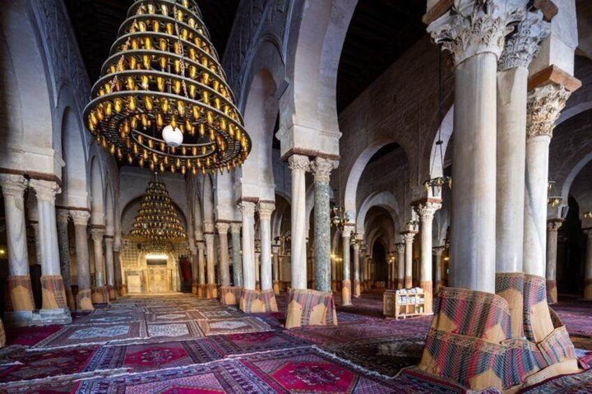 An interior with a large, ornate chandelier, arches, and patterned carpet. 3