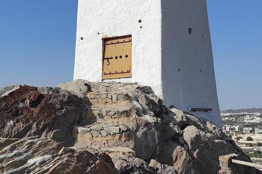 A white tower with a wooden door, rocky terrain, and a distant cityscape. 3