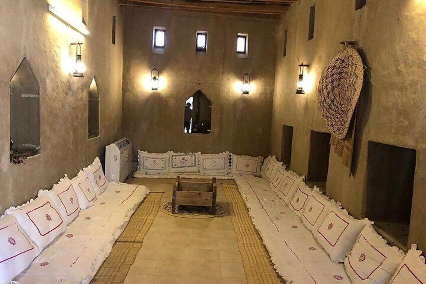 A traditional room with a long bench, wall-mounted lights, and a central rug. 2