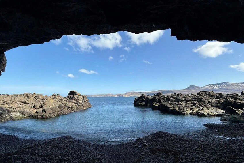 A rocky coastline with a cave entrance, calm sea, and distant mountains. 3