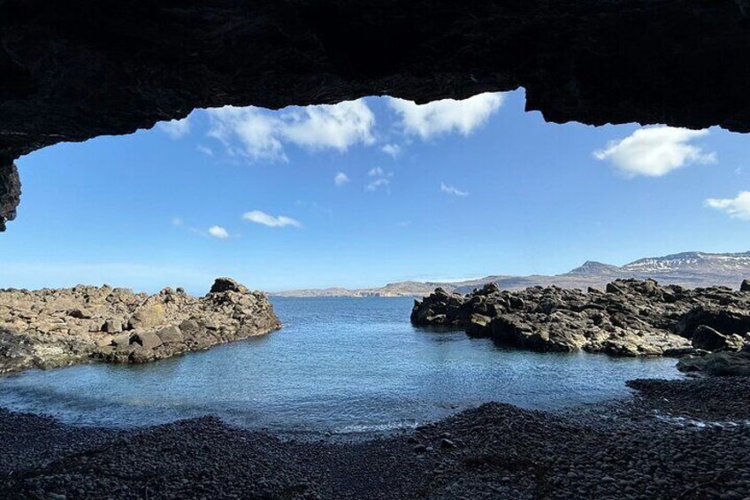 A rocky coastline with a cave entrance, calm sea, and distant mountains. 4