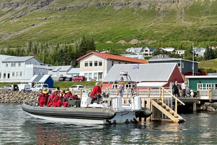 A boat with people in red suits, a dock, and houses in the background. 2