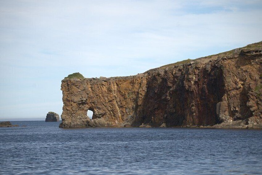 A coastal cliff with a natural arch formation and a smaller rock formation in the distance. 2