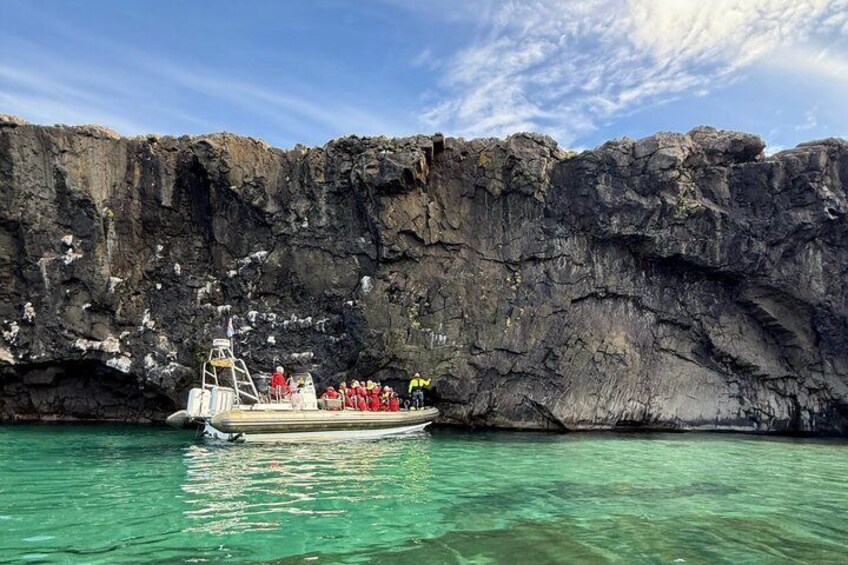 A boat with people in red life jackets near a rocky cliff. 1