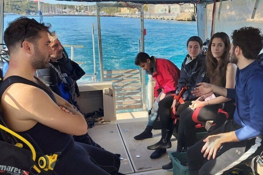 A group of people on a boat, some wearing diving gear, with a body of water and a dock in the background. 2