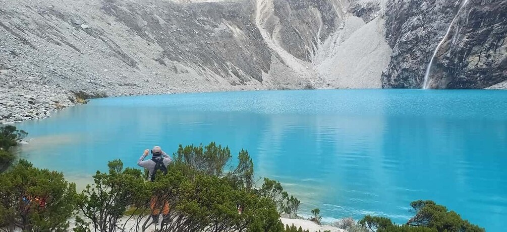A person taking a photo of a turquoise lake surrounded by rocky mountains. 4