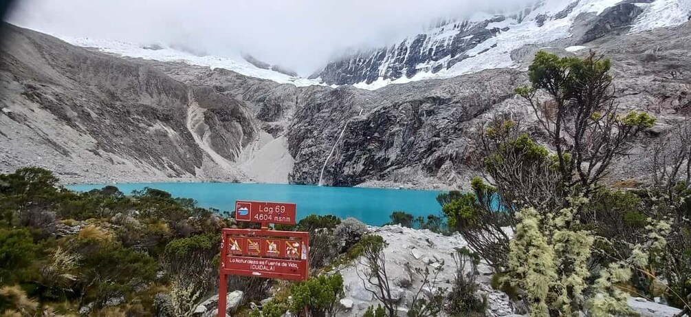 A mountain landscape with a turquoise lake, a sign indicating 'Lag 69' and '4604 msnm', and a trail sign with symbols. 3