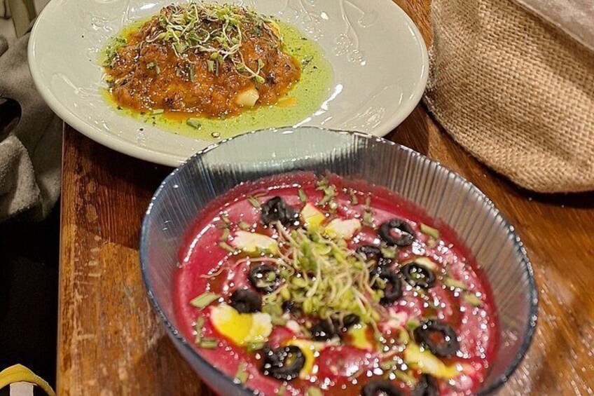 A wooden table with two dishes: one with a red sauce and green garnish, and another with a red sauce and black olives. 4