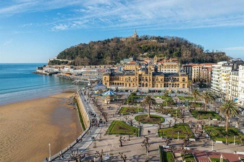 A coastal cityscape with a beach, promenade, and historic buildings on a hill. 2
