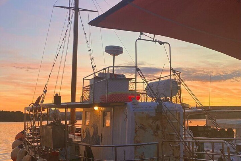 A boat docked at sunset with a red canopy, a mast, and various equipment on deck. 1