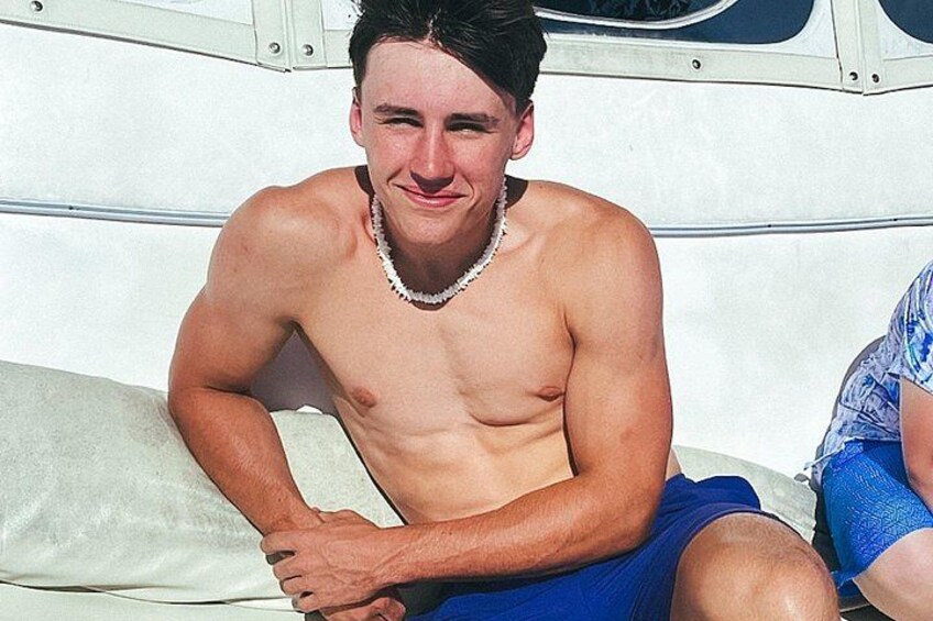 A shirtless man with a necklace sitting on a boat. 4