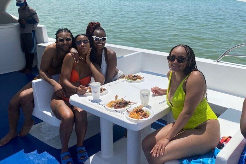 Three people sitting at a table on a boat with food and drinks. 5