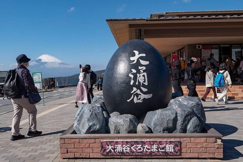 A large black sphere with Japanese characters, surrounded by rocks, in a public space with people walking around. 3