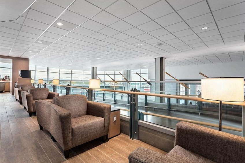 A modern airport lounge with seating, a glass railing, and a view of the airport terminal. 5