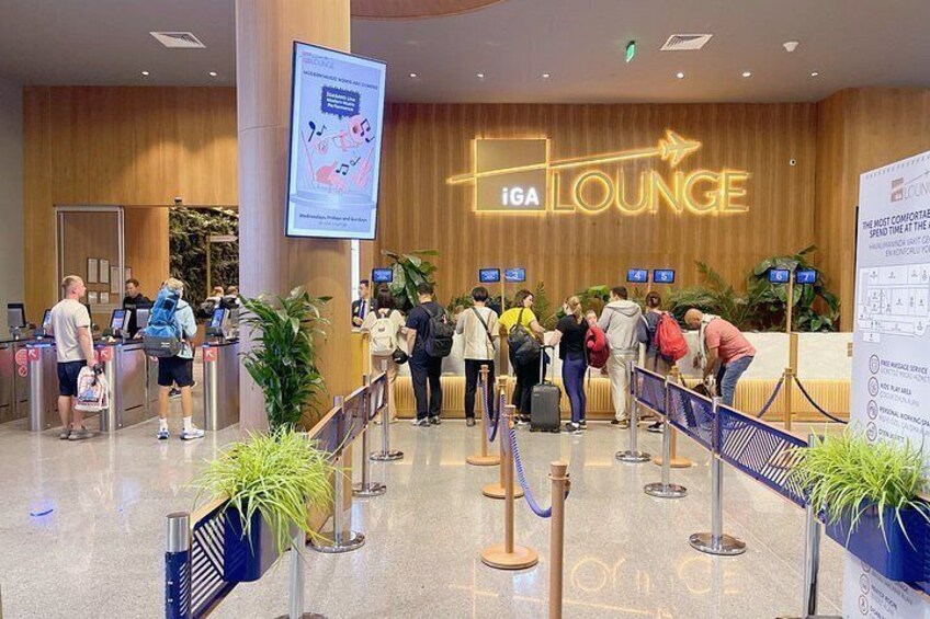 Eine Schlange vor einer iGA Lounge, Menschen warten, eine digitale Anzeige zeigt Informationen. 2