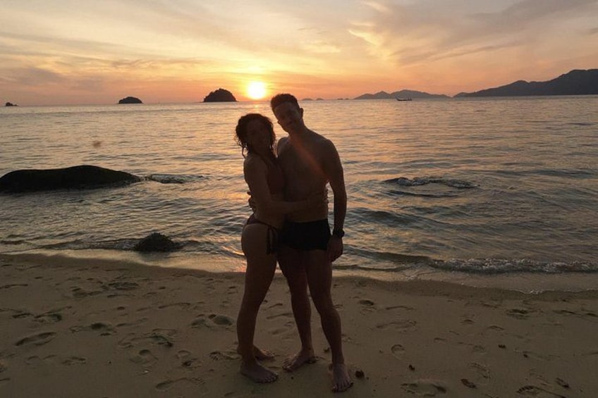 Een stel staat op het strand bij zonsondergang, met de zon die in de oceaan verdwijnt. 3