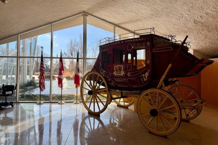 A vintage stagecoach in a museum with large windows and American flags. 2