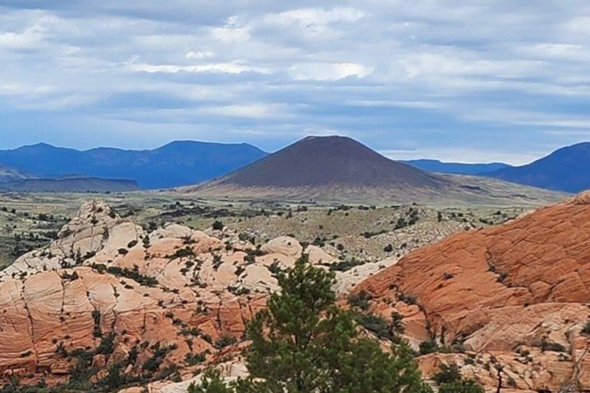 Eine gebirgige Landschaft mit roten Felsformationen und einem entfernten Berggipfel unter einem bewölkten Himmel. 4