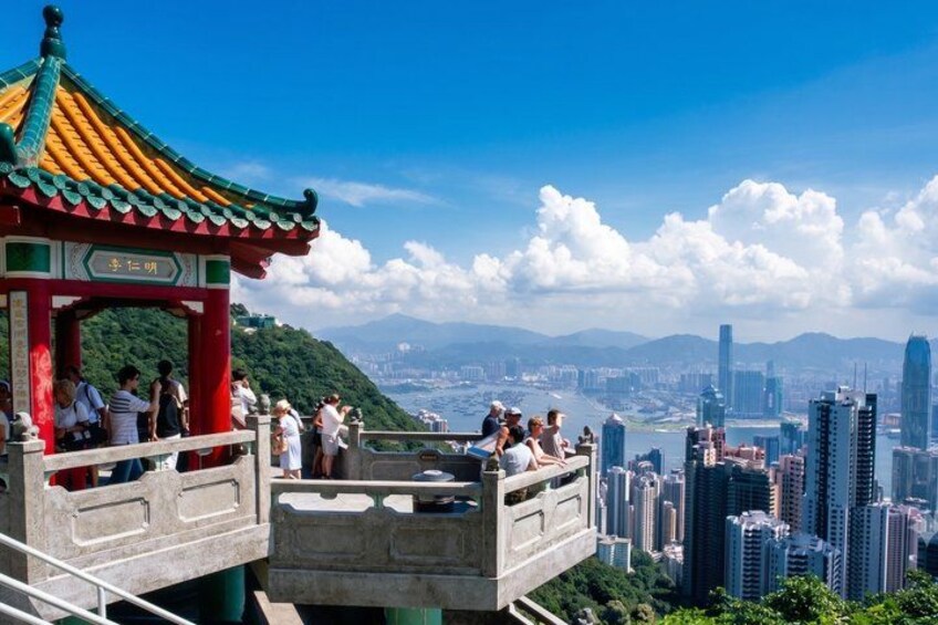A traditional Chinese pavilion with tourists, overlooking a cityscape with high-rise buildings and a distant mountain range. 1