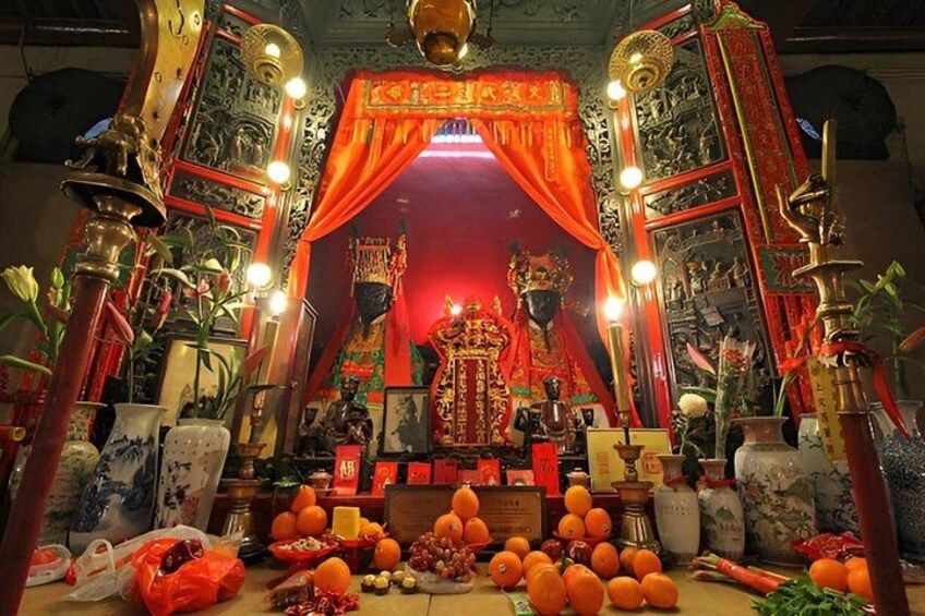 A shrine with a red curtain, ornate decorations, and offerings like oranges and flowers. 2