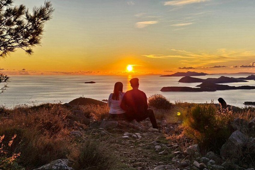 Tramonto su uno specchio d'acqua con la sagoma di una coppia seduta su una scogliera. 4
