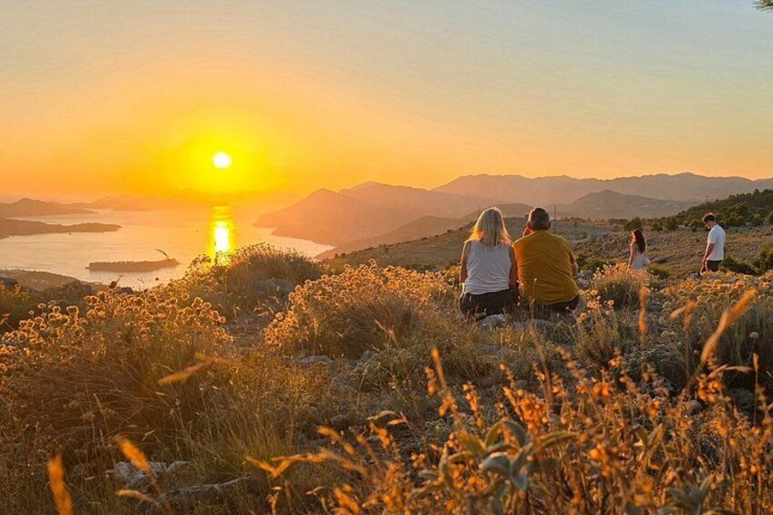 Tramonto su un paesaggio montuoso con persone sedute e in piedi su una collina erbosa. 3