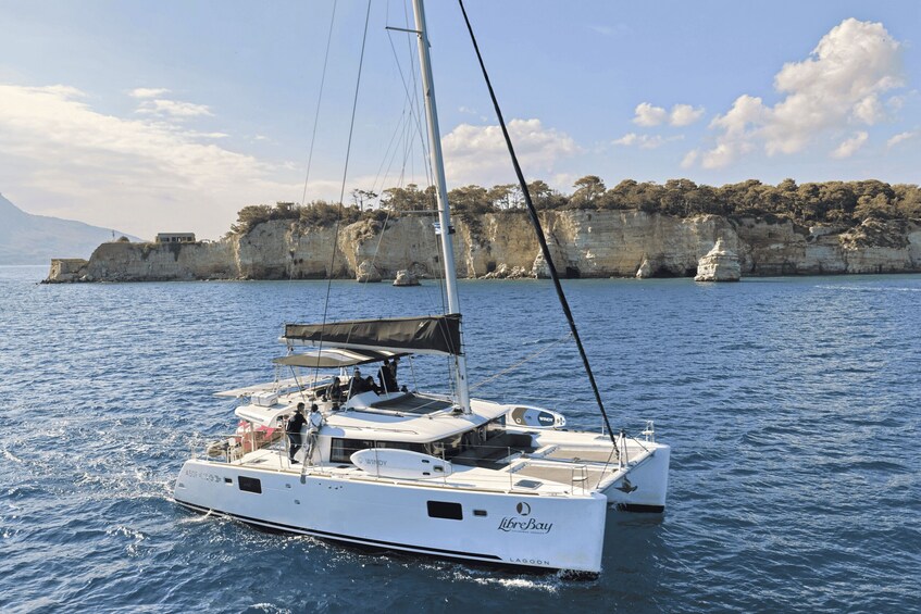 A white sailboat named 'LibeBay' on calm waters with a rocky coastline and cliffs in the background. 1