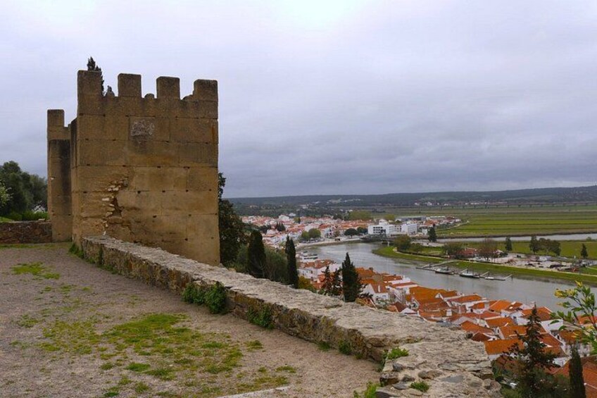 A historic stone tower, a river, and a town with red-roofed buildings. 3