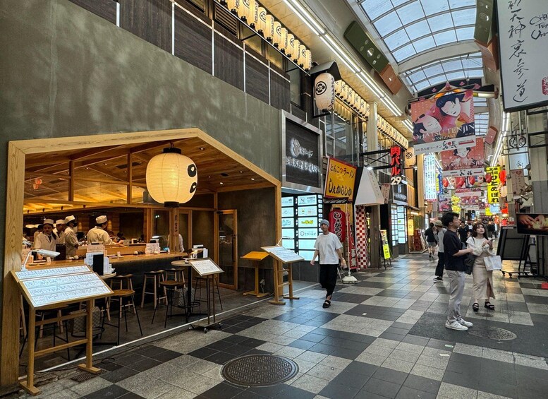 A bustling indoor market with a sushi restaurant, wooden interiors, and various signs in a foreign language. 2