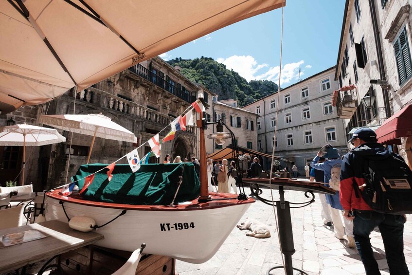 A small boat with the registration KT-1994 docked in a narrow street with buildings and a mountainous backdrop. 3