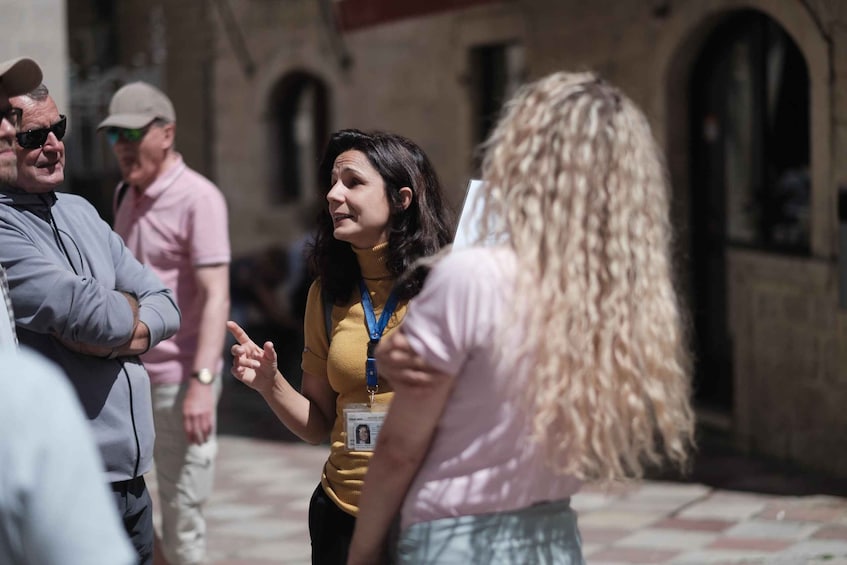 A group of people standing in an outdoor area with stone buildings and arches in the background. 4