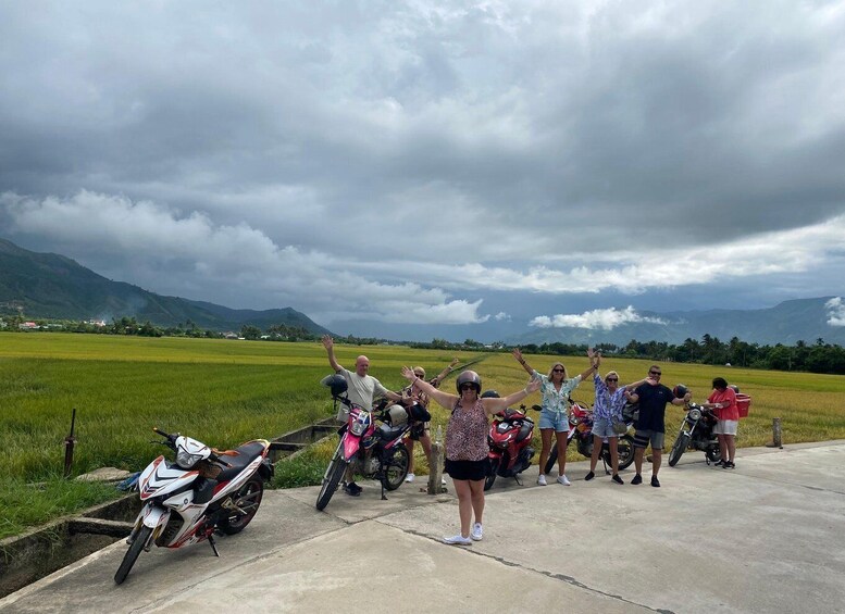 A group of people on motorcycles in a rural area with green fields and mountains in the background. 4