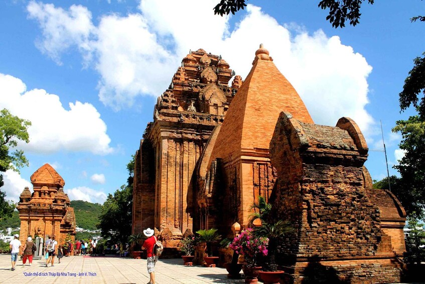 A large, ancient brick temple with multiple spires and intricate carvings, surrounded by tourists and potted plants. 1